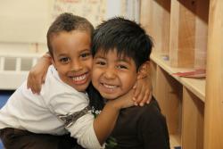 Two young boys of color embrace and small into the camera.
