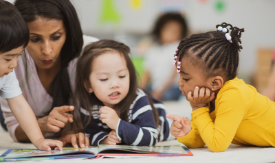 A teacher guides children reading a book.